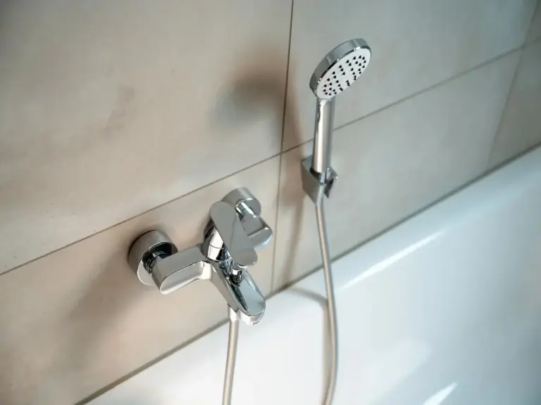 Modern bathtub fixture and handheld shower head in tiled bathroom