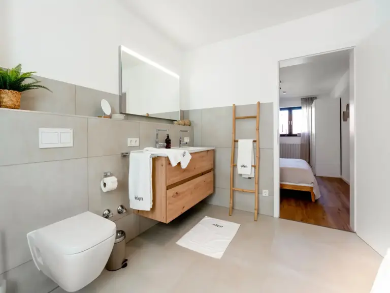 Modern bathroom with wooden vanity and view into bedroom in Opal White apartment
