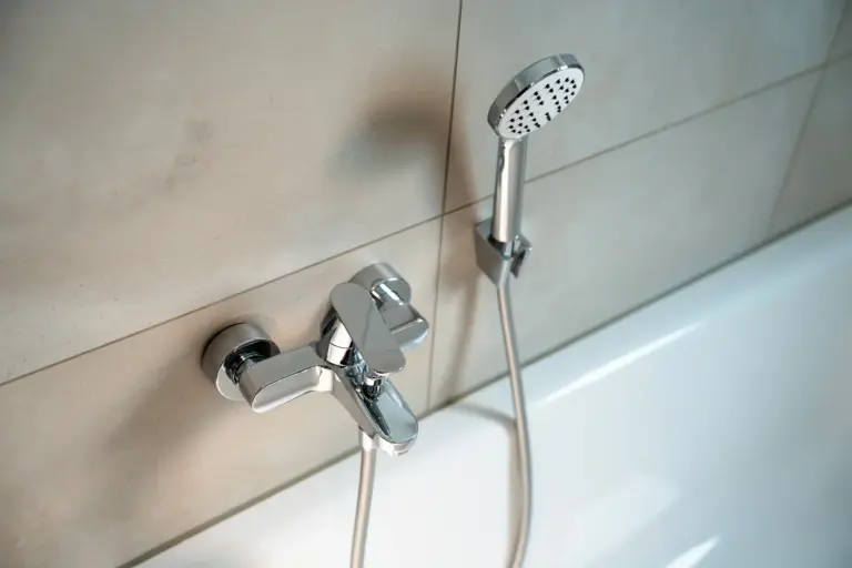 Modern bathtub fixture and handheld shower head in tiled bathroom