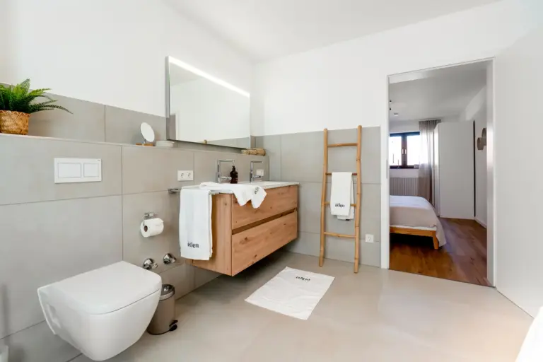 Modern bathroom with wooden vanity and view into bedroom in Opal White apartment
