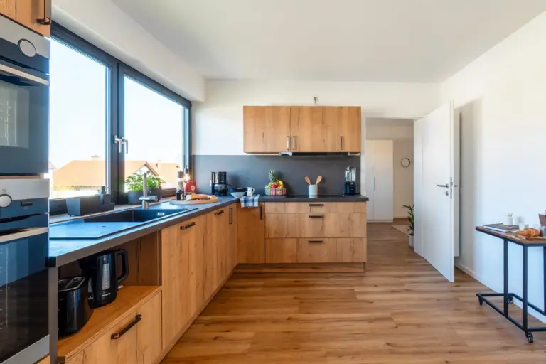 Spacious kitchen with wood cabinetry and large windows in Opal White apartment
