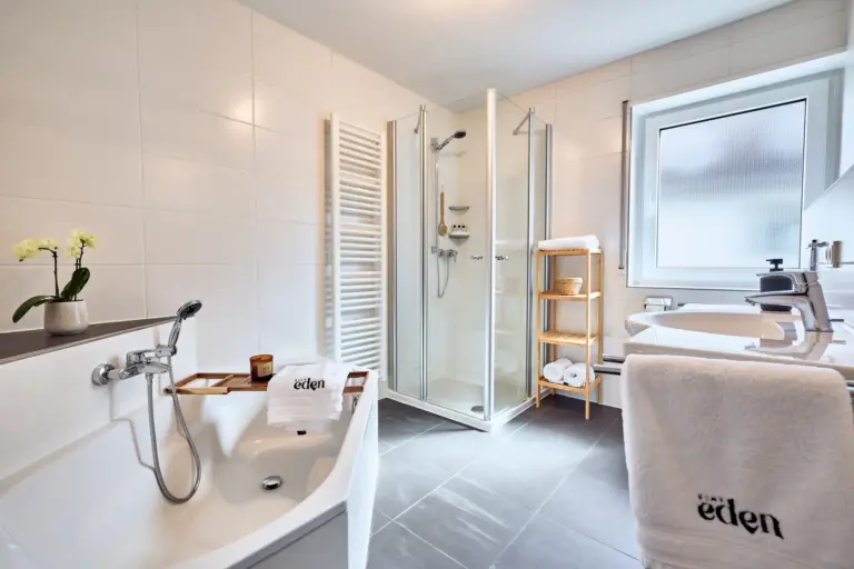 Bright CORAL BLOOM bathroom with bathtub, glass shower, heated towel rack and white towels