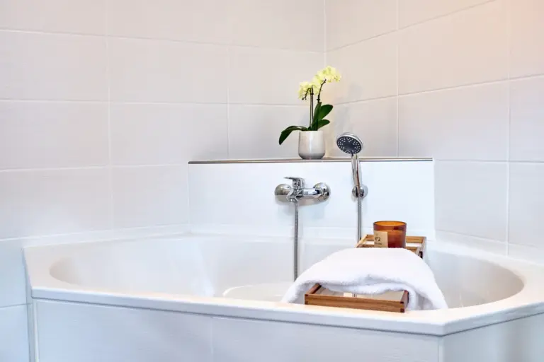 Corner bathtub in CORAL BLOOM's bright bathroom with towel, candle and orchid
