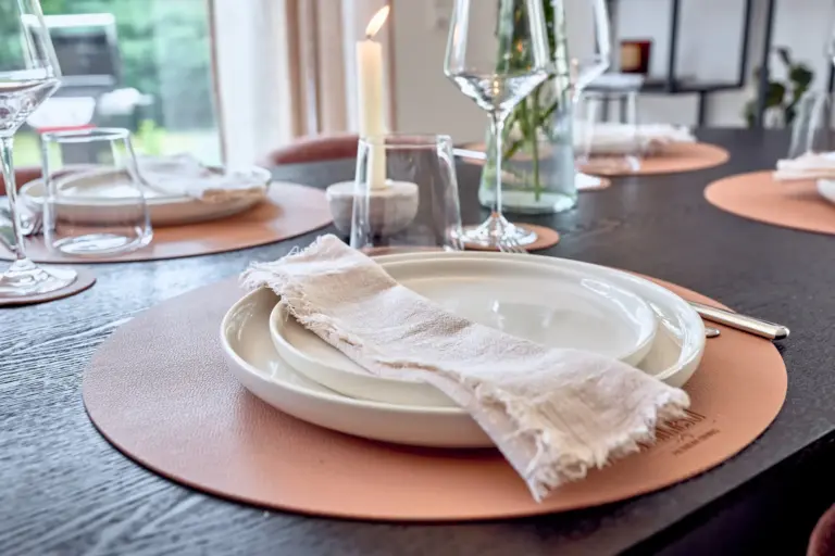 Elegant table setting with ceramic plates, linen napkin and warm-toned placemat at CORAL BLOOM