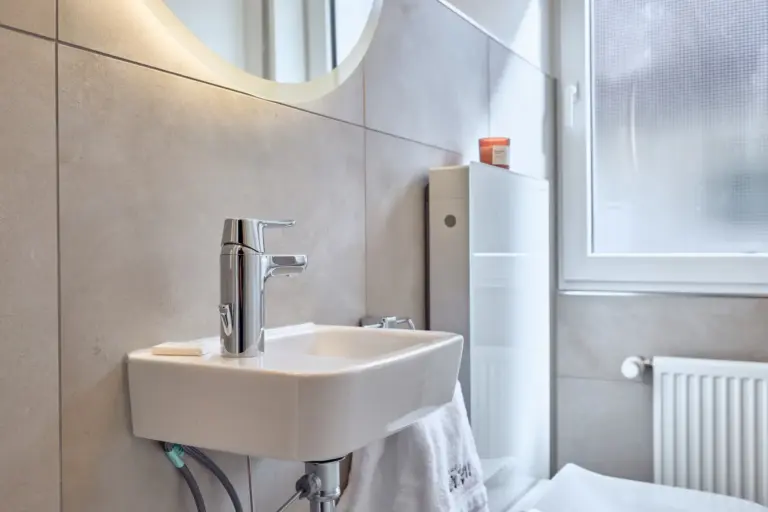 Compact washbasin in CORAL BLOOM's half bath with chrome faucet and illuminated round mirror