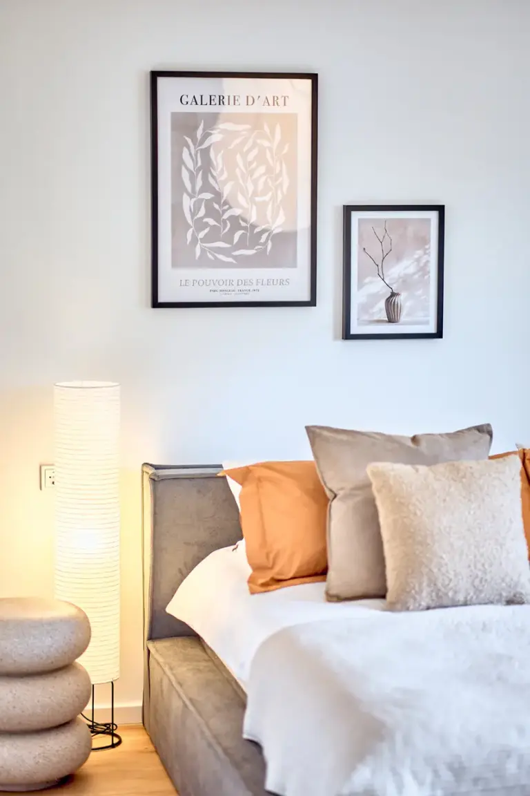 Master bedroom at CORAL BLOOM with upholstered bed, warm coral cushions, framed wall art and softly illuminated floor lamp