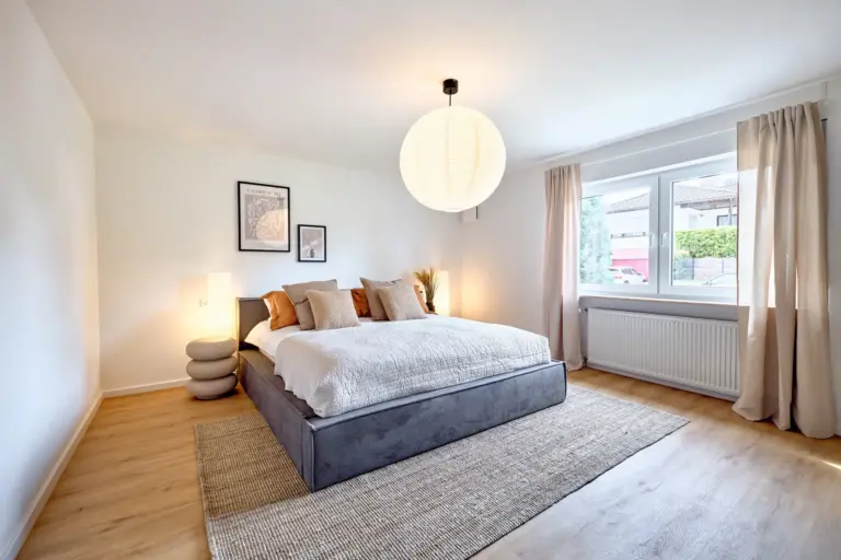 Spacious master bedroom at CORAL BLOOM with large upholstered bed, warm ambient lighting, neutral decor and natural daylight
