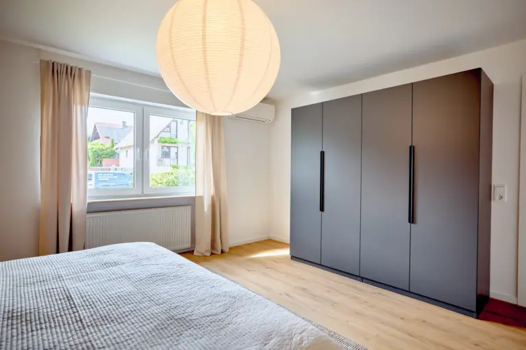 Master bedroom at CORAL BLOOM with large dark wardrobe, natural daylight, neutral curtains and warm wood flooring
