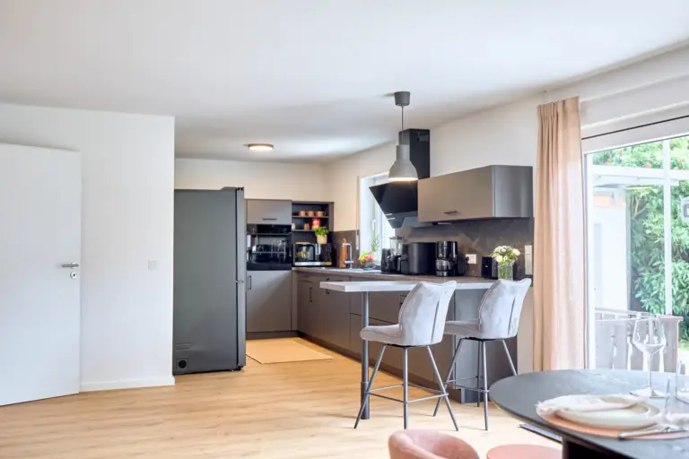 CORAL BLOOM modern kitchen with dark cabinetry, breakfast bar, two bar chairs and garden access