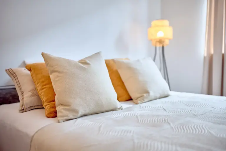 Comfortable bed with layered cushions in warm neutral tones and soft ambient lighting in CORAL BLOOM's bedroom