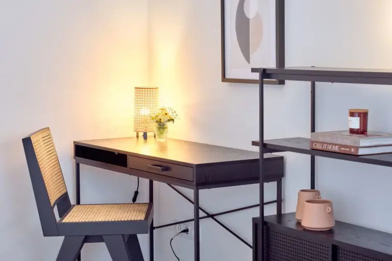 Dedicated workspace at CORAL BLOOM with dark wood desk, woven chair, warm table lamp and decorative shelving