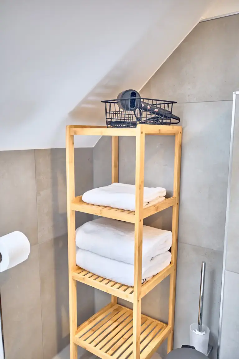 Wooden bathroom shelf in CORAL SUN with neatly folded white towels and hairdryer