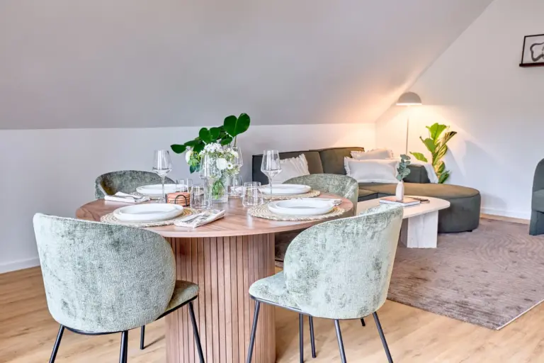 Dining and lounge area in CORAL SUN with round wooden table, four green chairs and spacious corner sofa