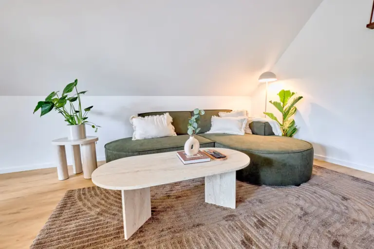 Green sectional sofa in CORAL SUN with white cushions, oval coffee table, textured rug and surrounding plants