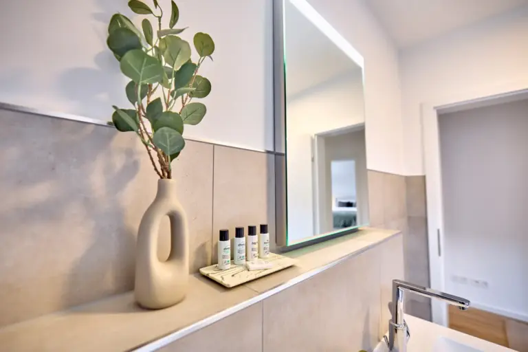 Illuminated bathroom mirror in CORAL SUN with toiletries and vase