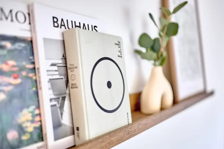 Close-up of design books and decorative vase with greenery on a wooden shelf in the CORAL SUN living room
