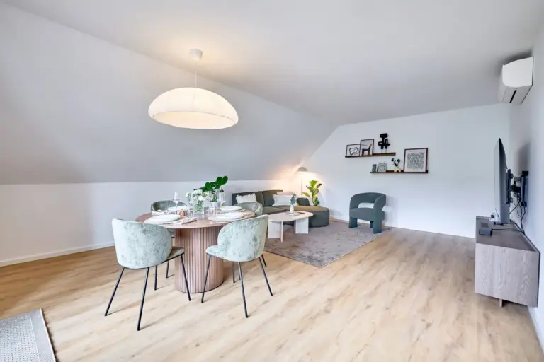 Spacious CORAL SUN living and dining area with round dining table, green seating and wall-mounted TV