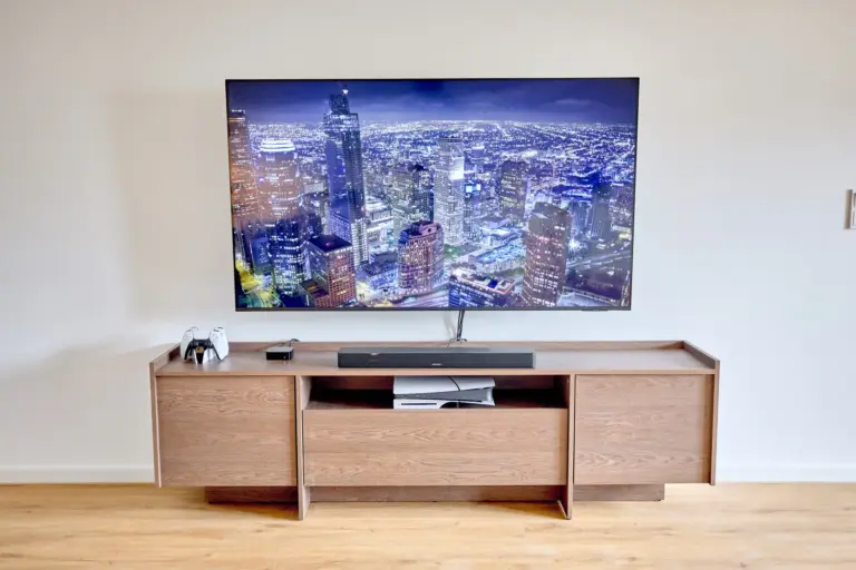 Large wall-mounted TV in CORAL SUN with soundbar, PlayStation 5, controllers and Apple TV on a wooden media console