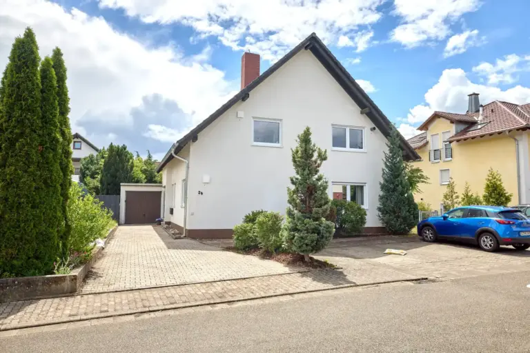 Front view of CORAL with white facade, driveway, garage and surrounding greenery